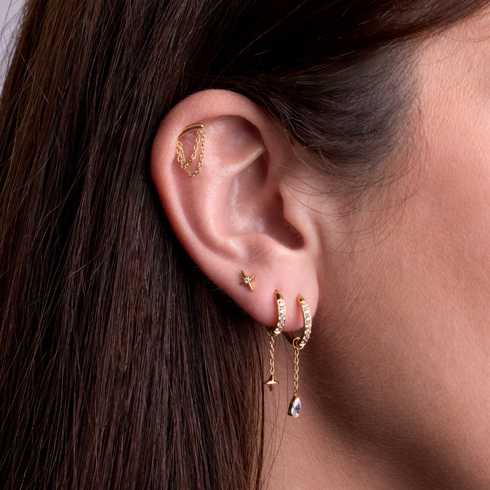Bijoux de piercing en titane à l'oreille, collection Mocha classiques: Eclissi à l'hélix, Ristretto blanc en 3ème lobe, Oriel blanc 8mm au deuxième lobe orné d'un charm Cometa gold, Oriel blanc 10mm au 1er lobe orné d'un charm Mocaccino blanc.